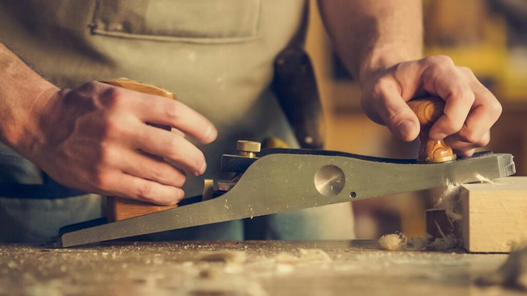 pexels-photo-374861-374861 A carpenter skillfully using a hand plane on a wooden surface indoors.